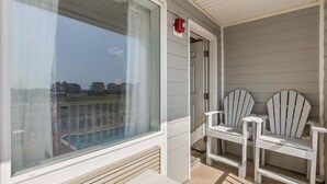 Ein Balkon mit Blick auf einen Swimmingpool, eine Tür und zwei Adirondack-Stühle.