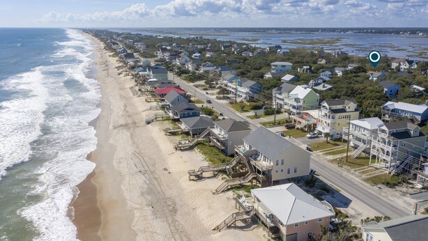 Un quartier résidentiel situé sur la côte, avec des maisons alignées le long de la plage, dont certaines offrent une vue directe sur l’océan.