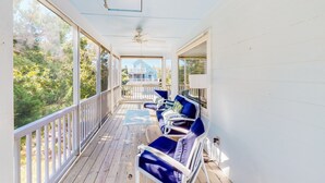 Une véranda couverte avec des balustrades blanches, des chaises rembourrées bleues et un ventilateur de plafond.