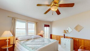 Un dormitorio con una cama grande, dos lámparas de noche, un ventilador de techo, un aparador y una silla.