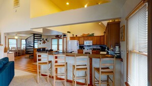 Una cocina amplia con una isla central, sillas de madera y una escalera que sube a un nivel superior.