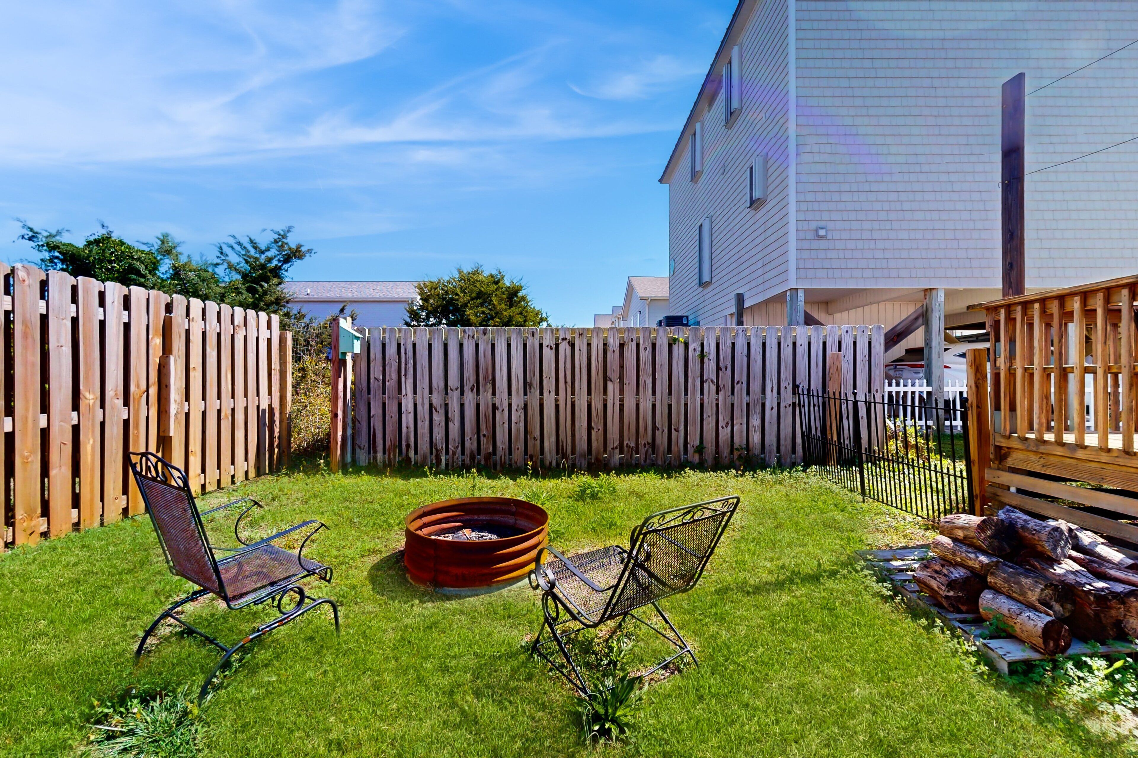 A backyard with two metal chairs, a fire pit, and a stack of logs.