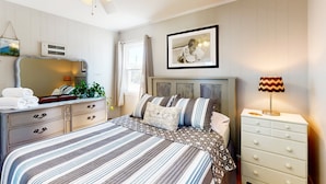 Une chambre à coucher avec un lit, une commode, un miroir et un ventilateur de plafond.