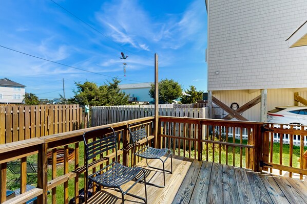 A wooden deck with metal chairs, a wooden fence, and a white building in the background. - Dog-friendly house with enclosed yard, deck space and short walk to beach (Surf City)