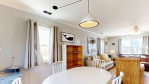 Un salon moderne avec une table à manger blanche, un canapé, un fauteuil en osier et une bibliothèque.