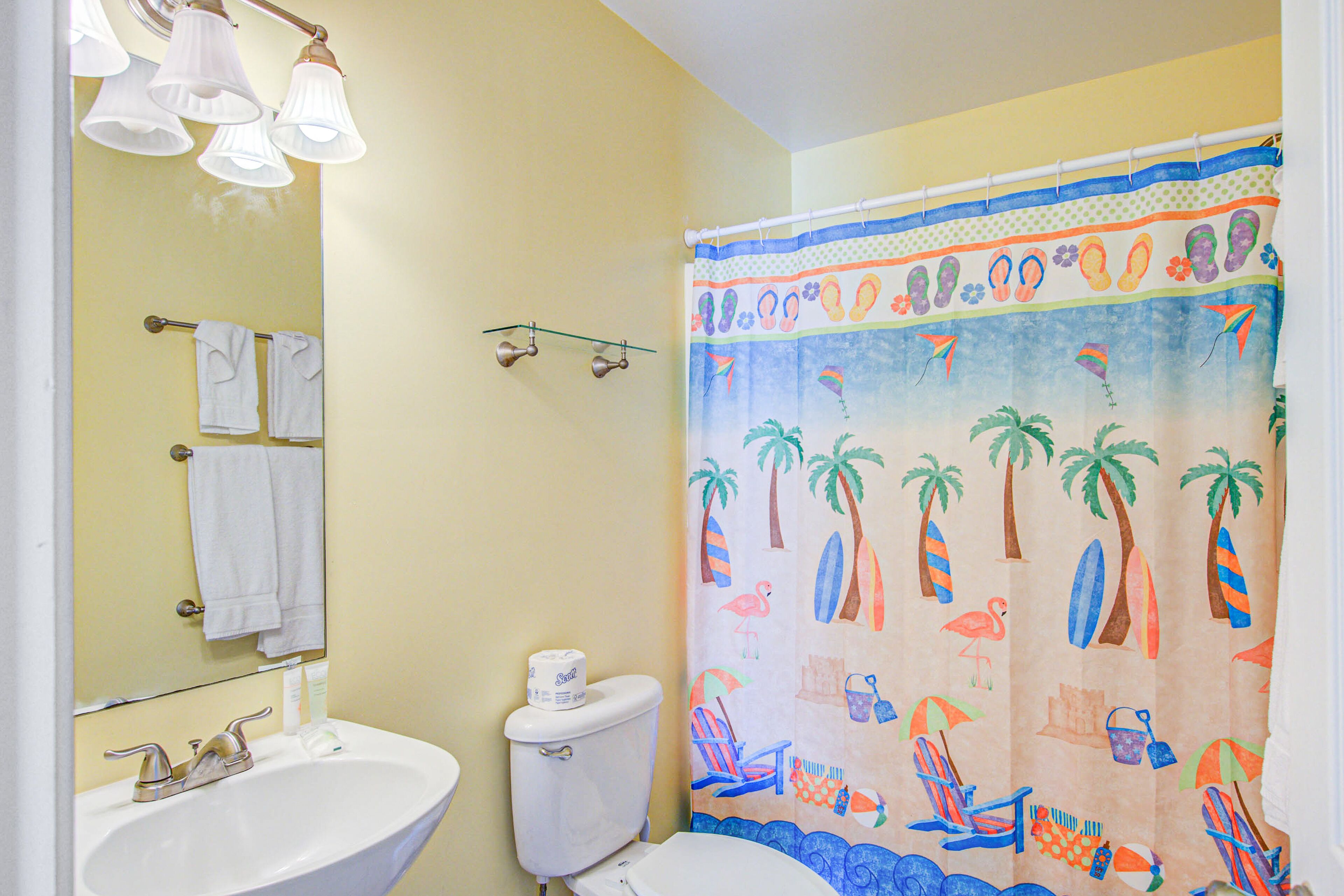 Une salle de bain avec un lavabo blanc, des toilettes et un rideau de douche à motifs de plage.