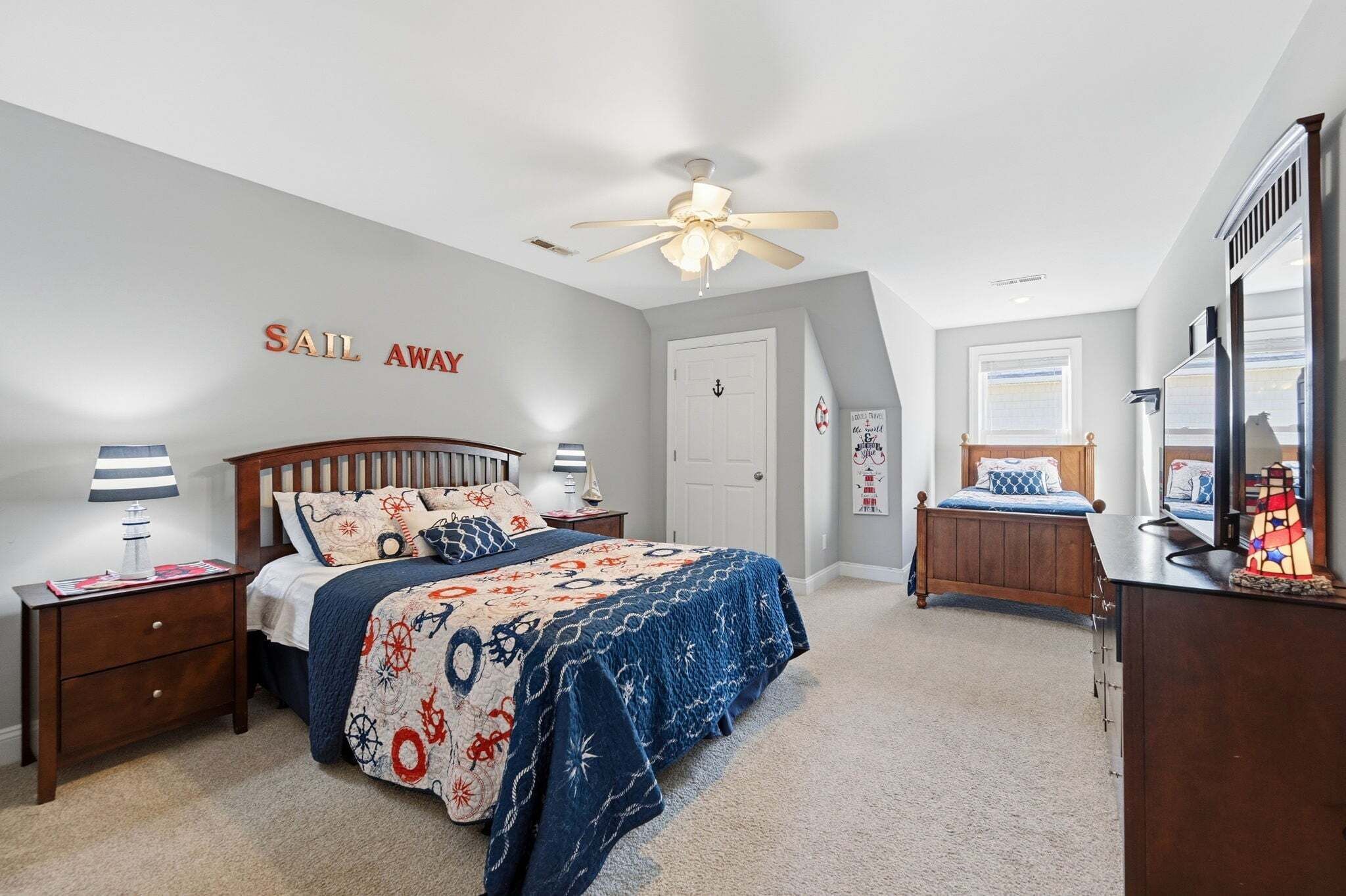 A bedroom with a bed, nightstands, a ceiling fan, a dresser, a mirror, and a wall with 'Sail Away' text.