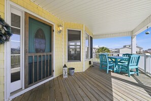 A covered porch with a table and chairs, a door with a decorative glass panel, and a lantern. - Family-Friendly Canal Home - Steps to the Beach (Surf City)