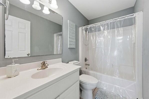 Un baño con lavamanos blanco, espejo, inodoro y cortina de ducha.
