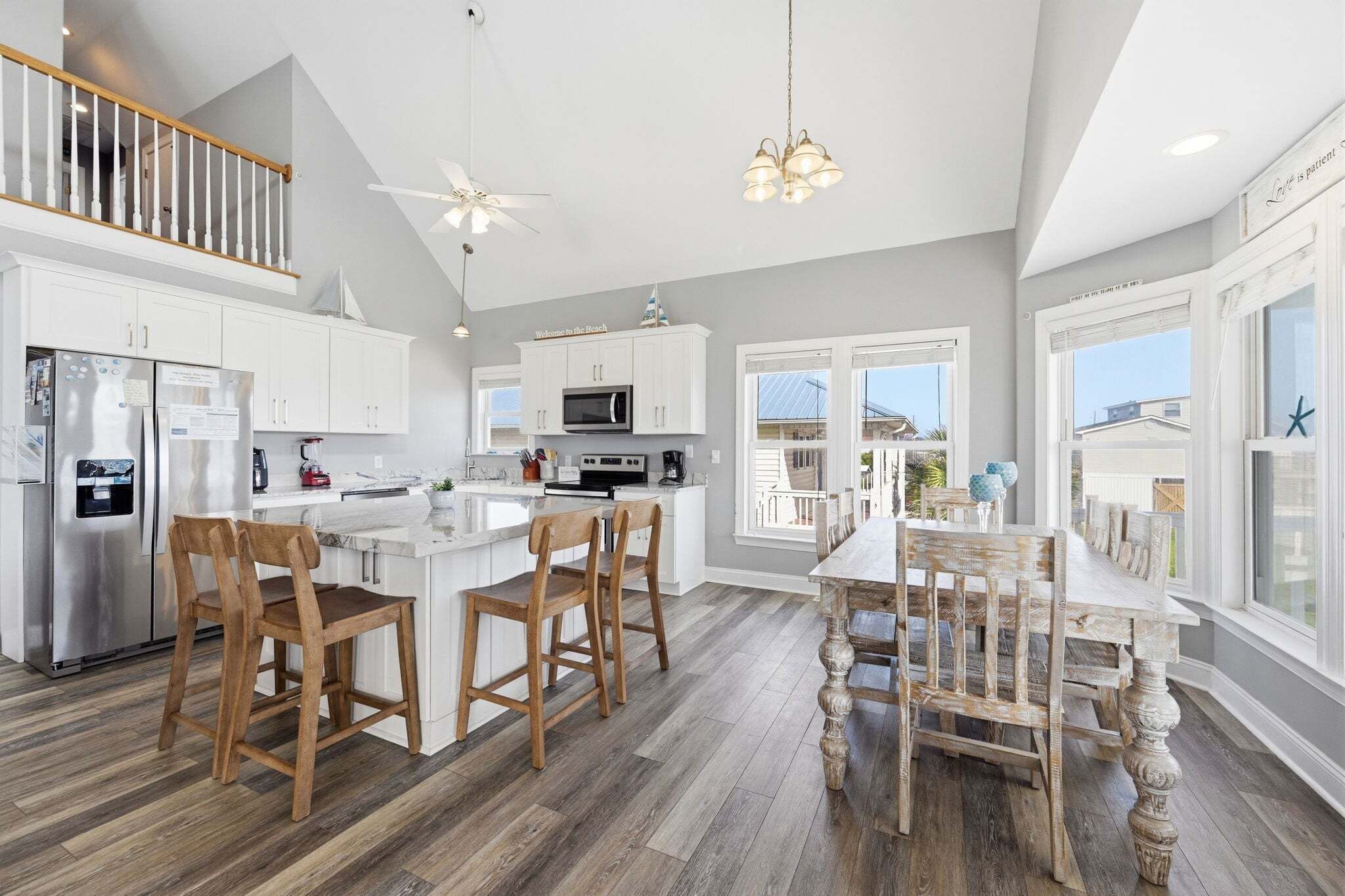 A modern kitchen with white cabinets, a stainless steel refrigerator, wooden chairs, and a dining table.