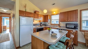 A kitchen with wooden cabinets, a white refrigerator, a microwave, and a large island with seating. - Dog-friendly home steps from the beach with deck, WiFi, AC & great location (Buxton)