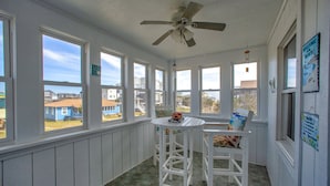 A sunroom with large windows, a ceiling fan, and a table with chairs. - Dog-friendly home steps from the beach with deck, WiFi, AC & great location (Buxton)