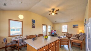 A spacious kitchen with a central island, wooden cabinets, and a dining area with chairs and a table. - Dog-friendly home steps from the beach with deck, WiFi, AC & great location (Buxton)