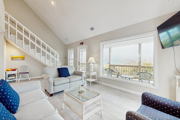 A spacious living room with a staircase, a large window with a view, and a flat-screen TV mounted on the wall.