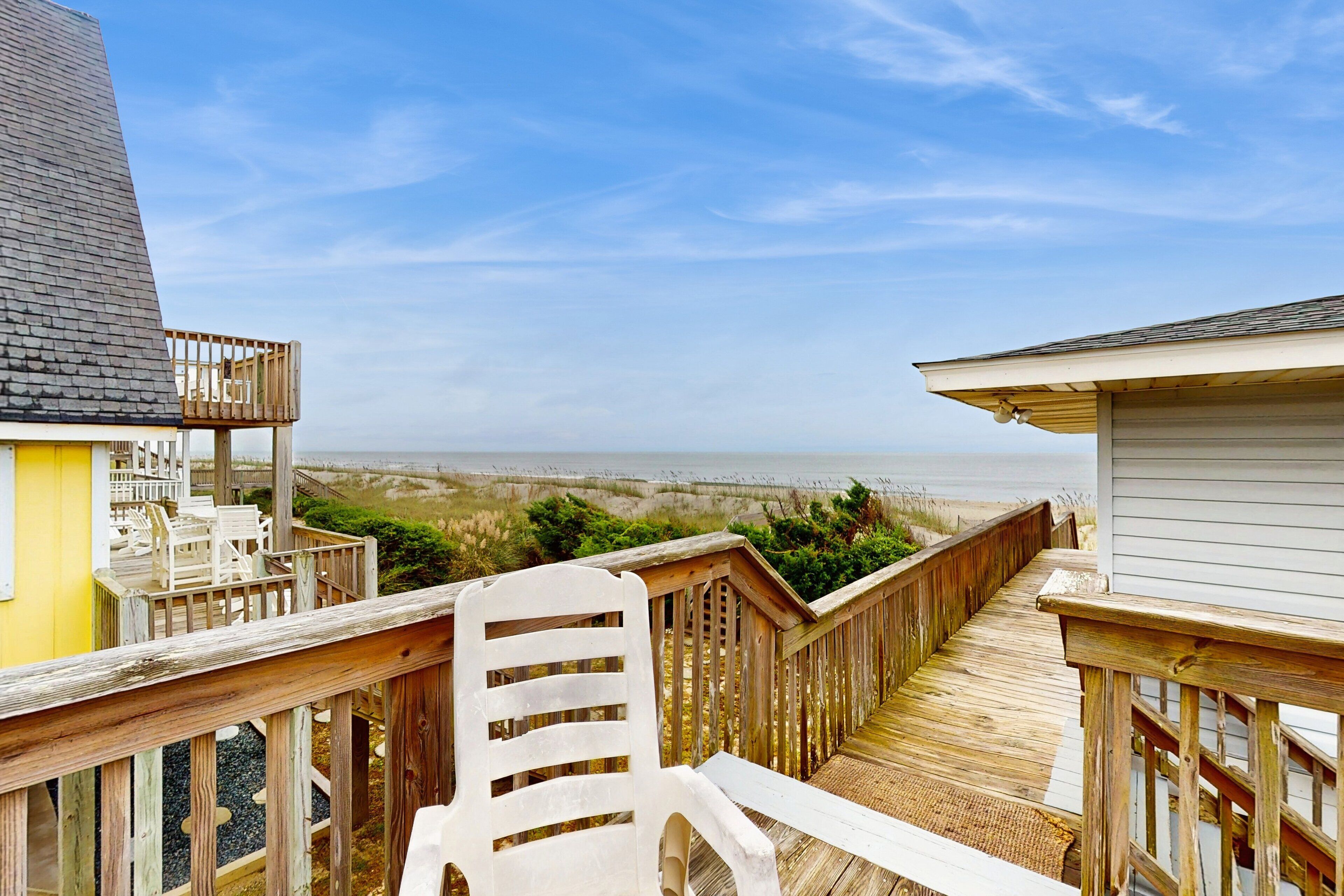 A wooden deck with a white chair, overlooking a beach and ocean.