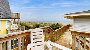 Une terrasse en bois avec une chaise blanche, donnant sur une plage et l’océan.