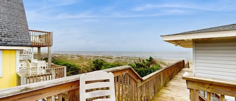Eine Holzterrasse mit einem weißen Stuhl, mit Blick auf einen Strand und das Meer.