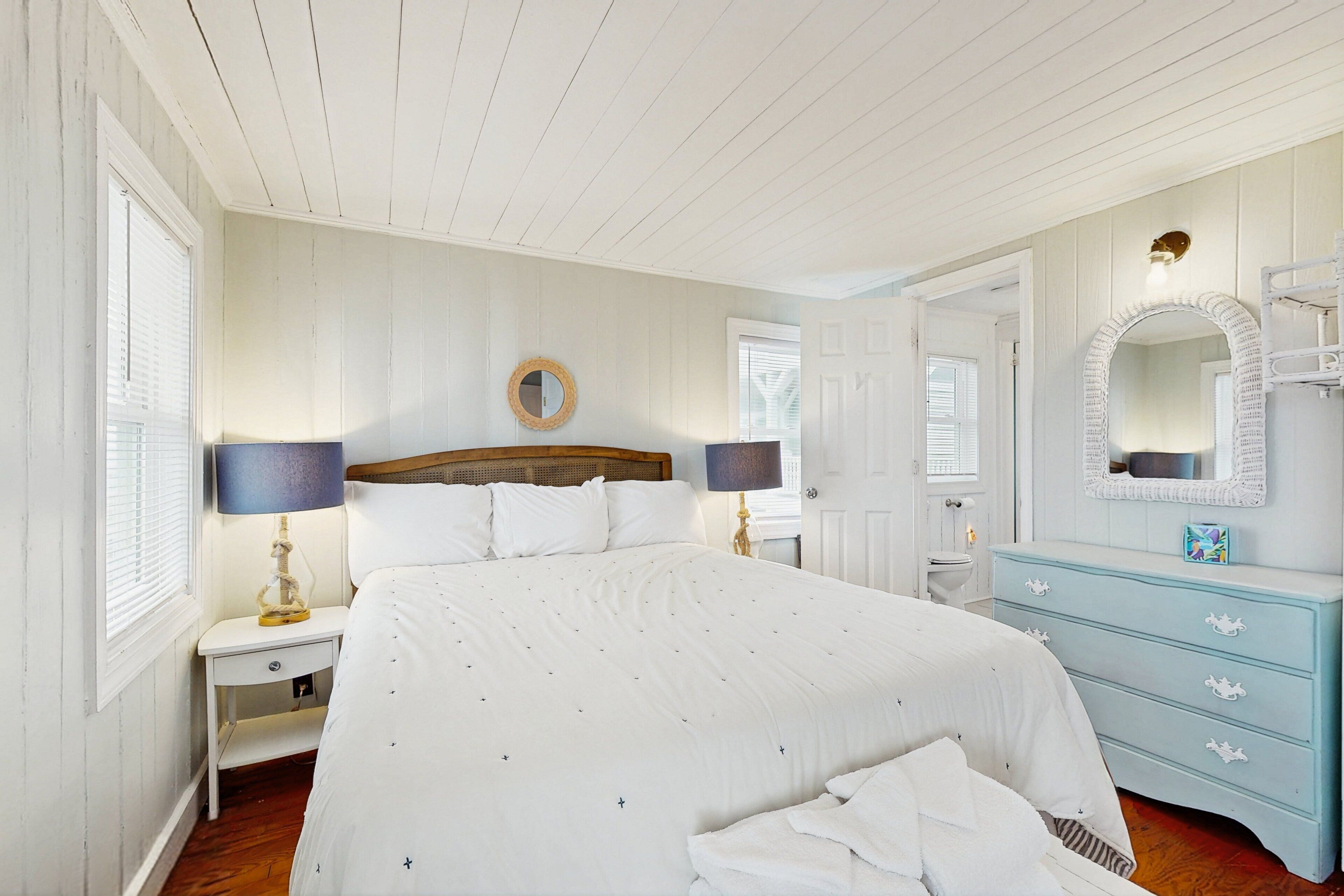 A bedroom with a large bed, two bedside tables with lamps, a dresser, and a mirror.