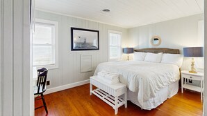 Une chambre à coucher avec un grand lit, un petit banc, une chaise et une table de chevet avec une lampe.