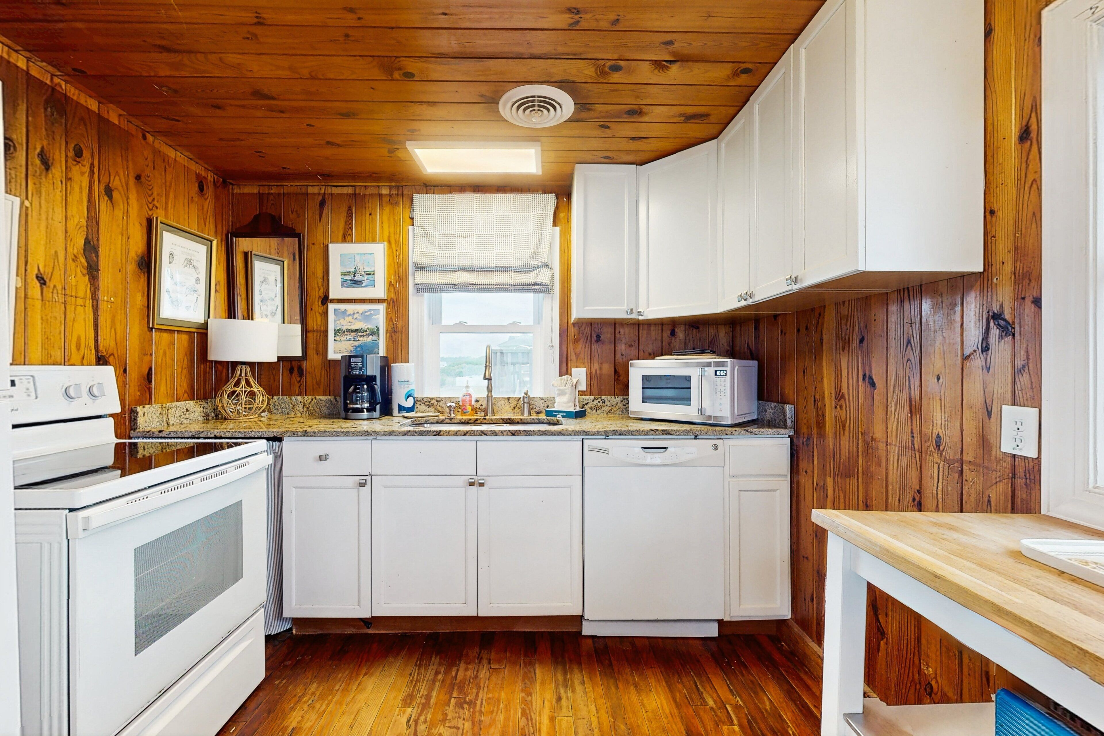 A kitchen with wooden walls, white cabinets, a microwave, a stove, and a dishwasher.