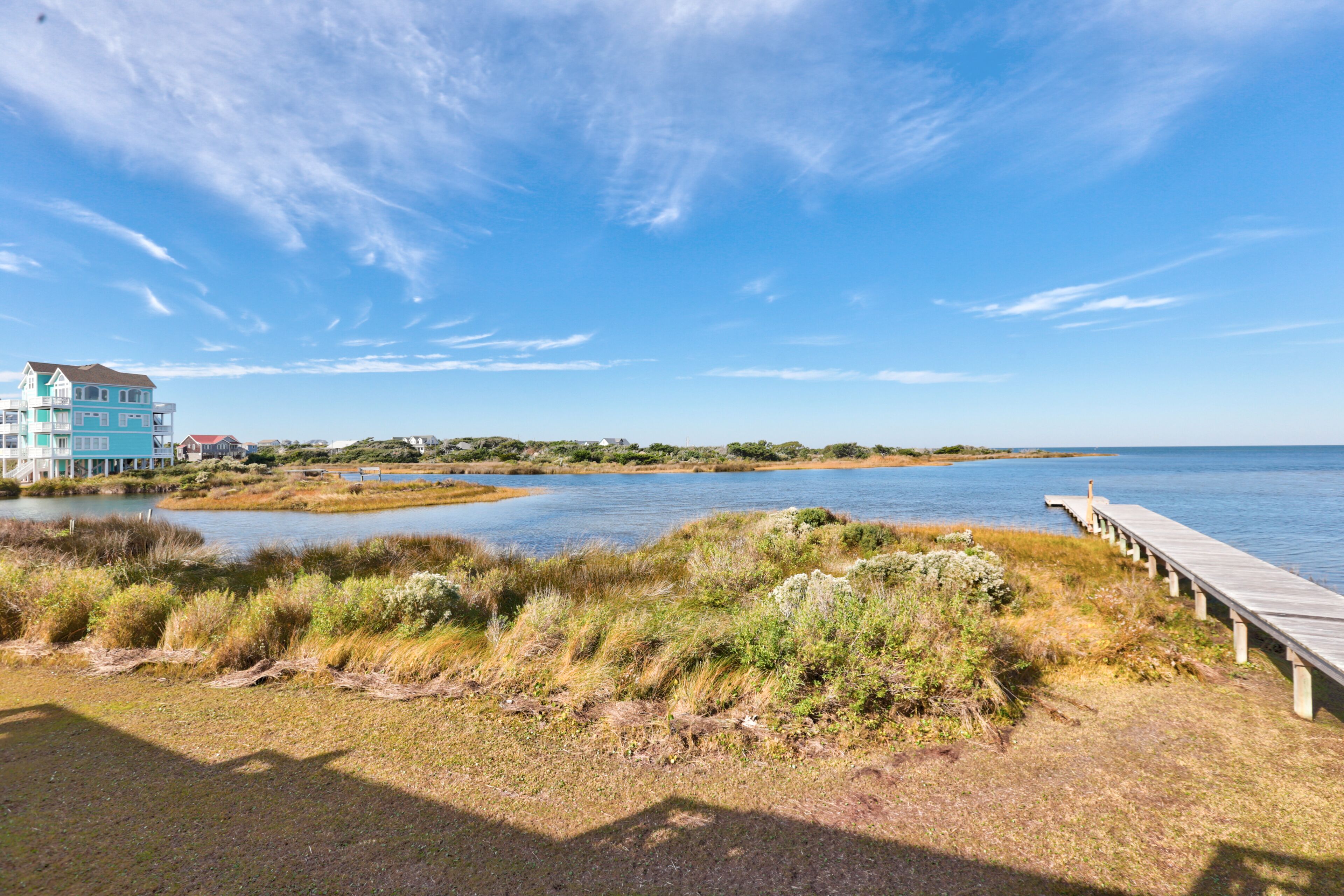 A coastal area with a wooden boardwalk leading to a body of water, a building with a blue facade, and a clear sky.