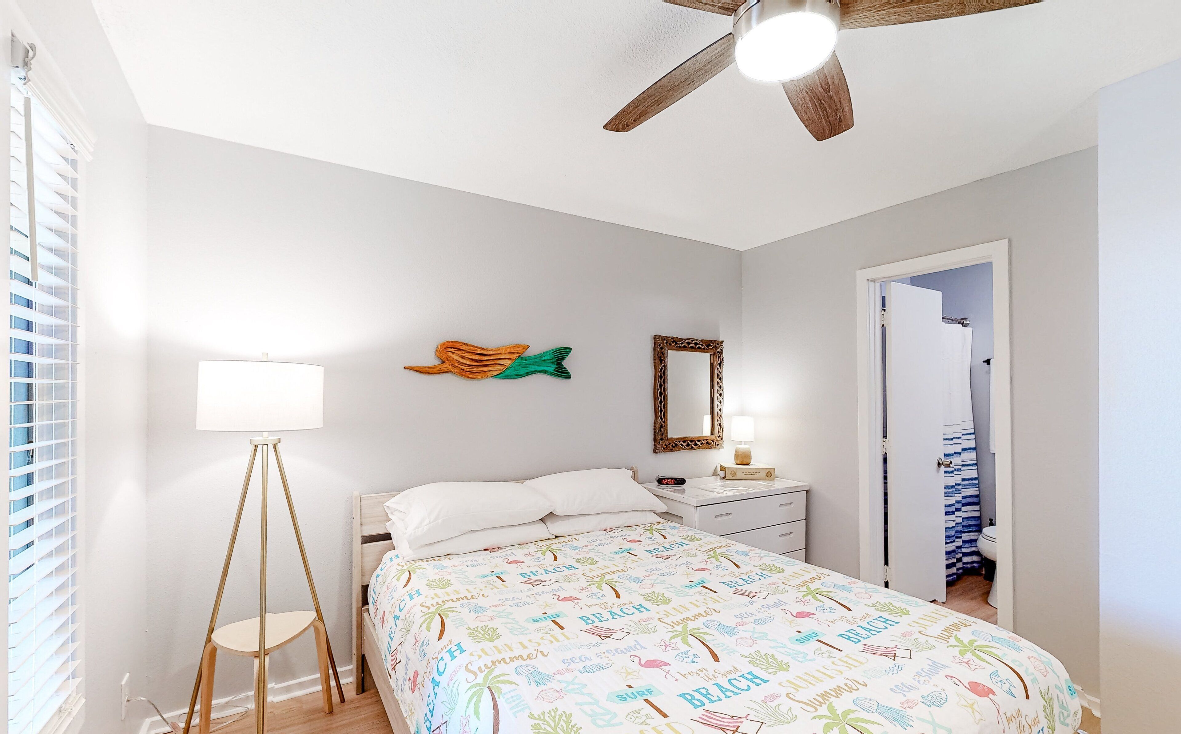 A bedroom with a bed, a bedside table, a lamp, a ceiling fan, and a window with blinds.
