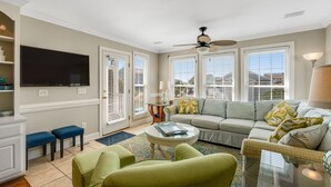 A living room with a sofa, two green armchairs, a coffee table, a flat-screen TV, and a ceiling fan. - Beautiful Waterway-View Home with Private Pool, Ping-Pong, Washer/Dryer & WiFi (Holden Beach)