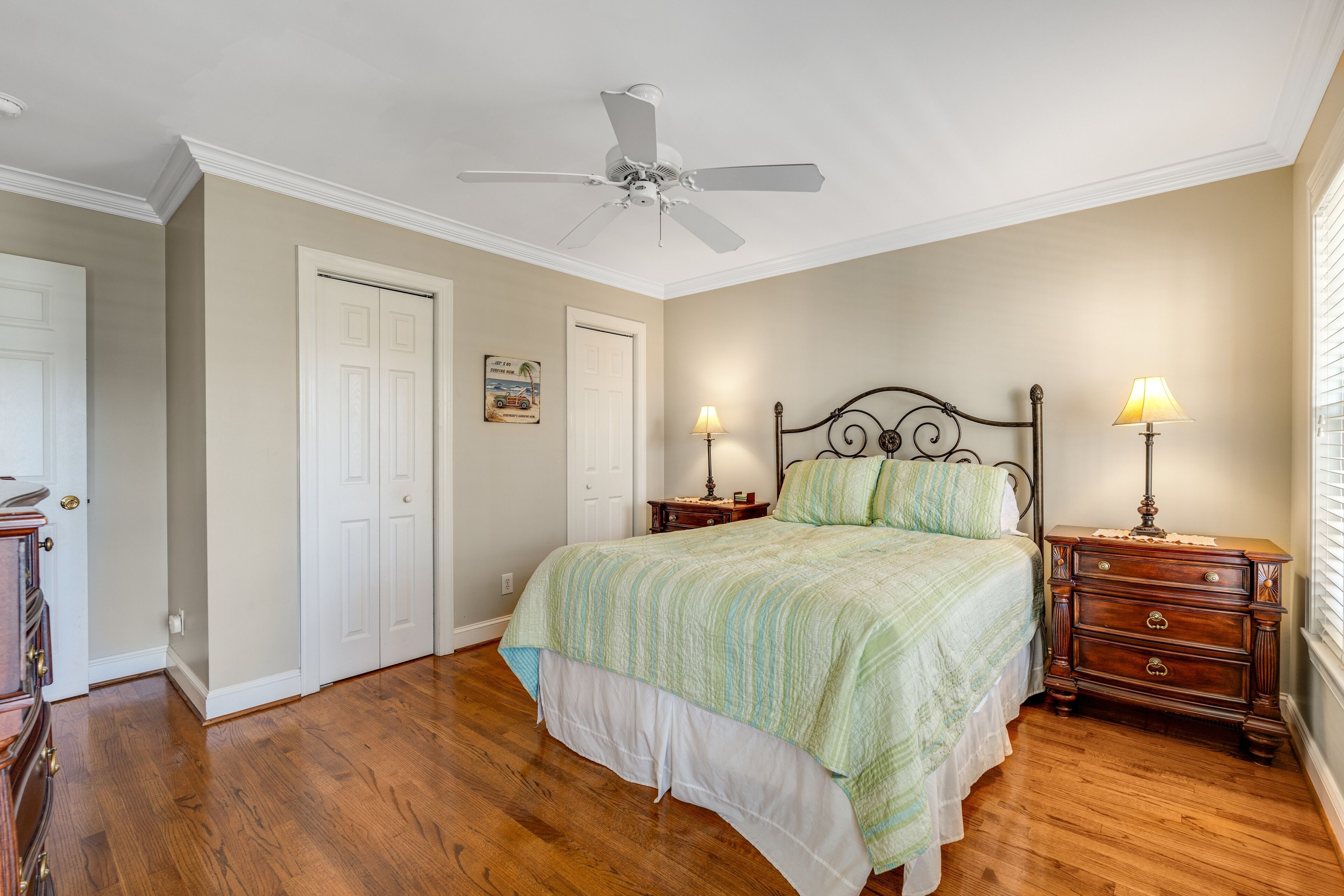 A bedroom with a bed, two bedside tables with lamps, a ceiling fan, and a door.