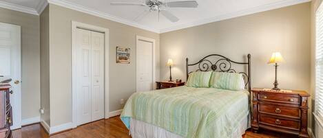 A bedroom with a bed, two bedside tables with lamps, a ceiling fan, and a door.