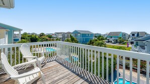 A wooden deck with white railings, two Adirondack chairs, and a view of a residential area with houses and a swimming pool. - Beautiful Waterway-View Home with Private Pool, Ping-Pong, Washer/Dryer & WiFi (Holden Beach)