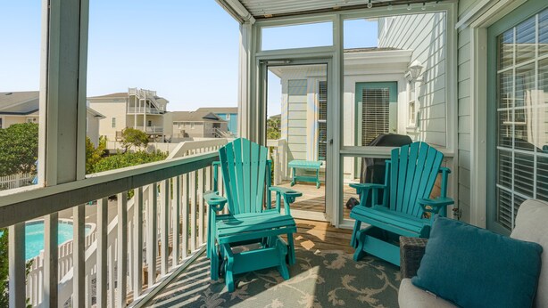 A covered porch with two turquoise Adirondack chairs, a small table, and a sofa with a cushion. - Beautiful Waterway-View Home with Private Pool, Ping-Pong, Washer/Dryer & WiFi (Holden Beach)