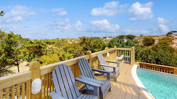 Un terrazzo in legno con poltrone Adirondack e una piscina.