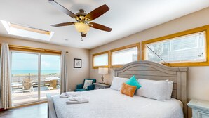 Una camera da letto con un letto grande, un ventilatore a soffitto e vista sulla spiaggia dalle finestre.