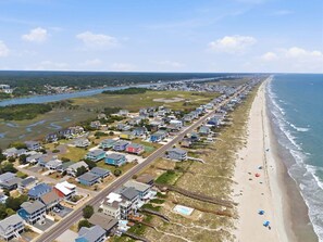An aerial view of a coastal residential area with houses, a beach, and a railway track.