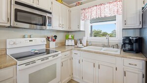 Una cocina con armarios blancos, microondas, horno, tostadora, pileta y cafetera.