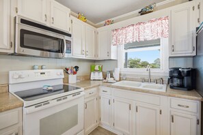A kitchen with white cabinets, a microwave, an oven, a toaster, a sink, and a coffee maker.
