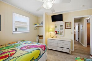 A bedroom with a bed, a dresser, a TV, a window with blinds, and a ceiling fan.