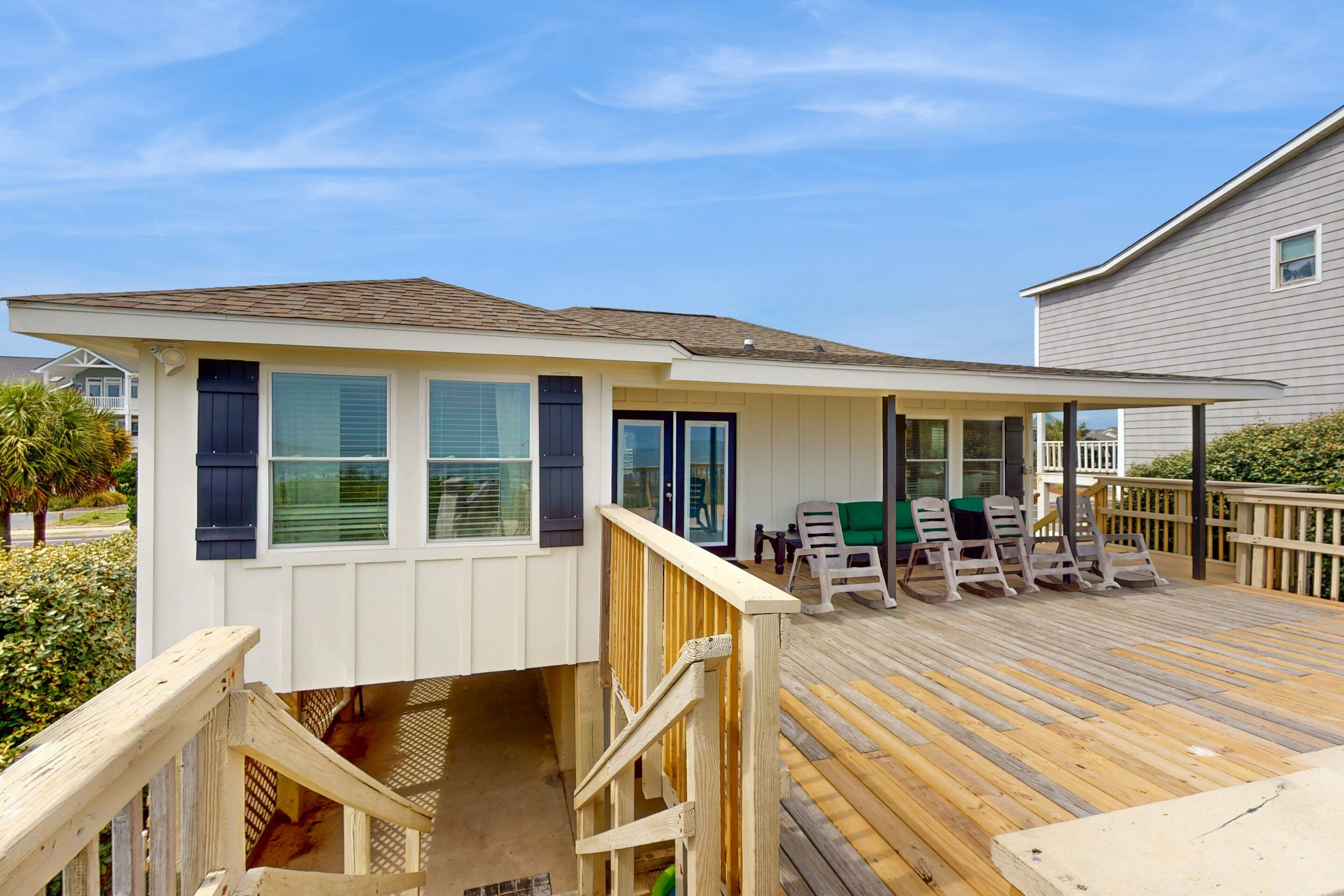 A deck with wooden railings, a covered seating area, and a small building with windows and shutters.