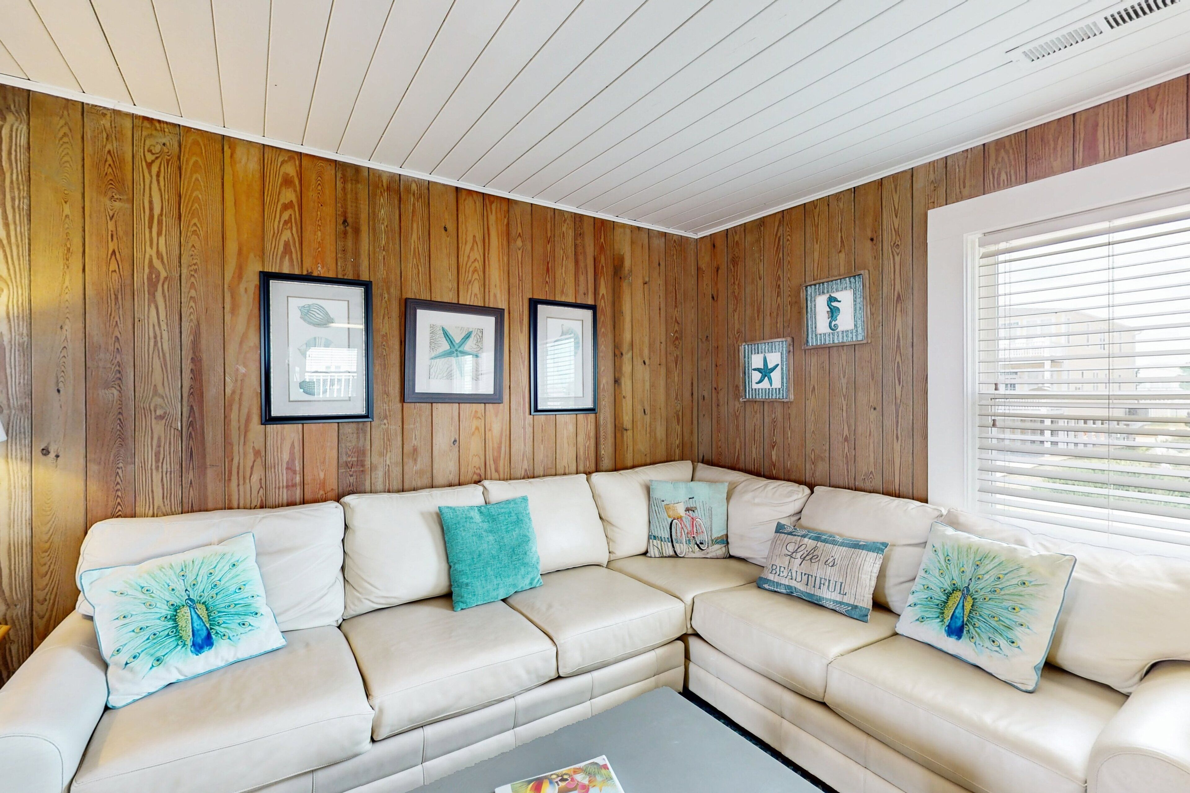 Un salon moderne avec un mur lambrissé en bois, un canapé d’angle beige et des œuvres d’art encadrées.
