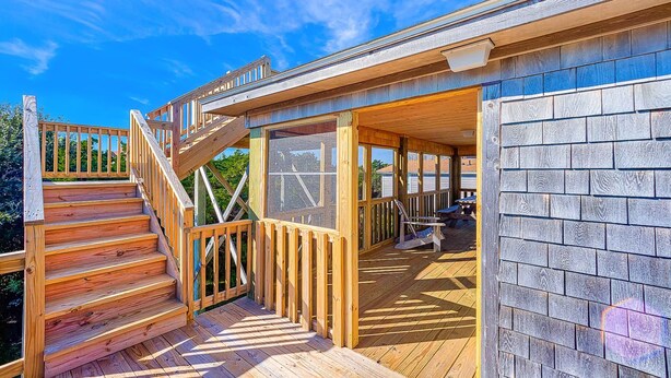 Una terraza de madera con una escalera que lleva a un espacio cubierto y vistas al cielo.