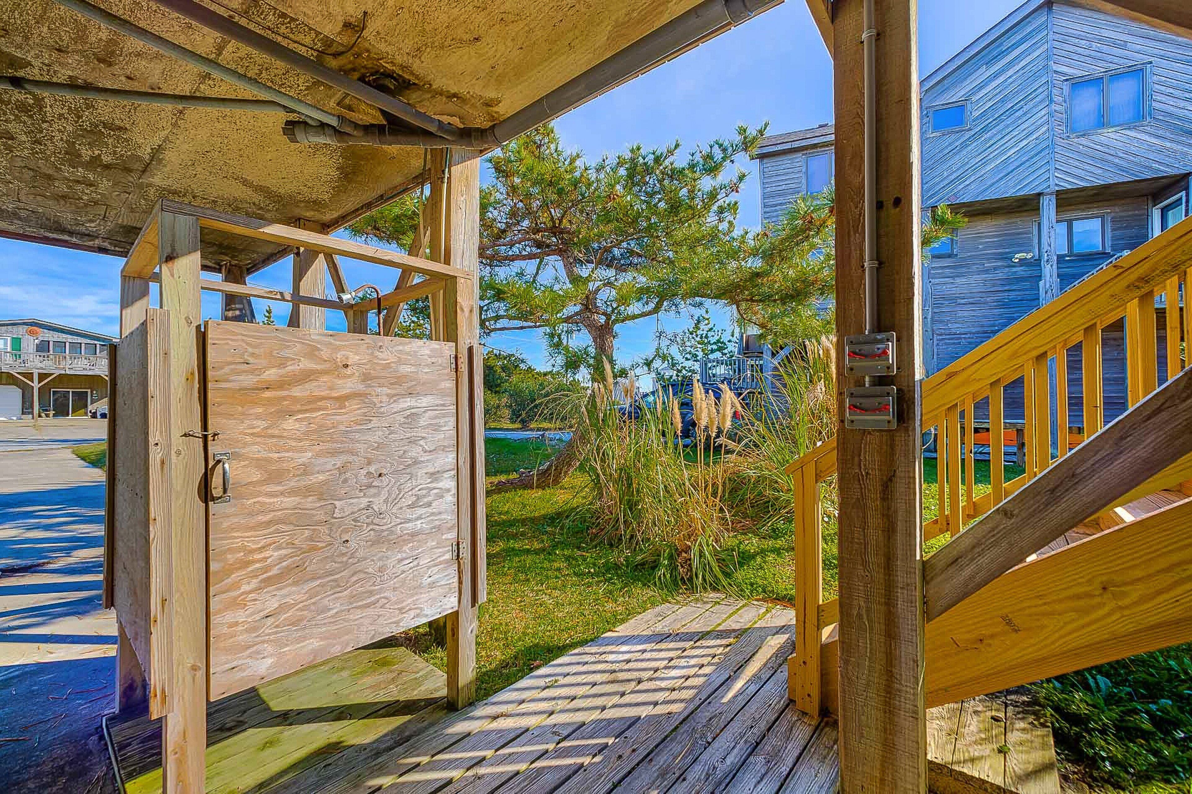 Une terrasse en bois avec une rambarde en métal, une porte en bois et un escalier menant à un bâtiment à la façade bleue.