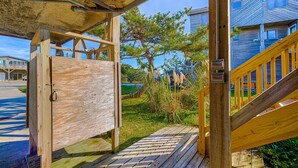 Una terraza de madera con baranda de metal, una puerta de madera y una escalera que lleva a un edificio de color azul.