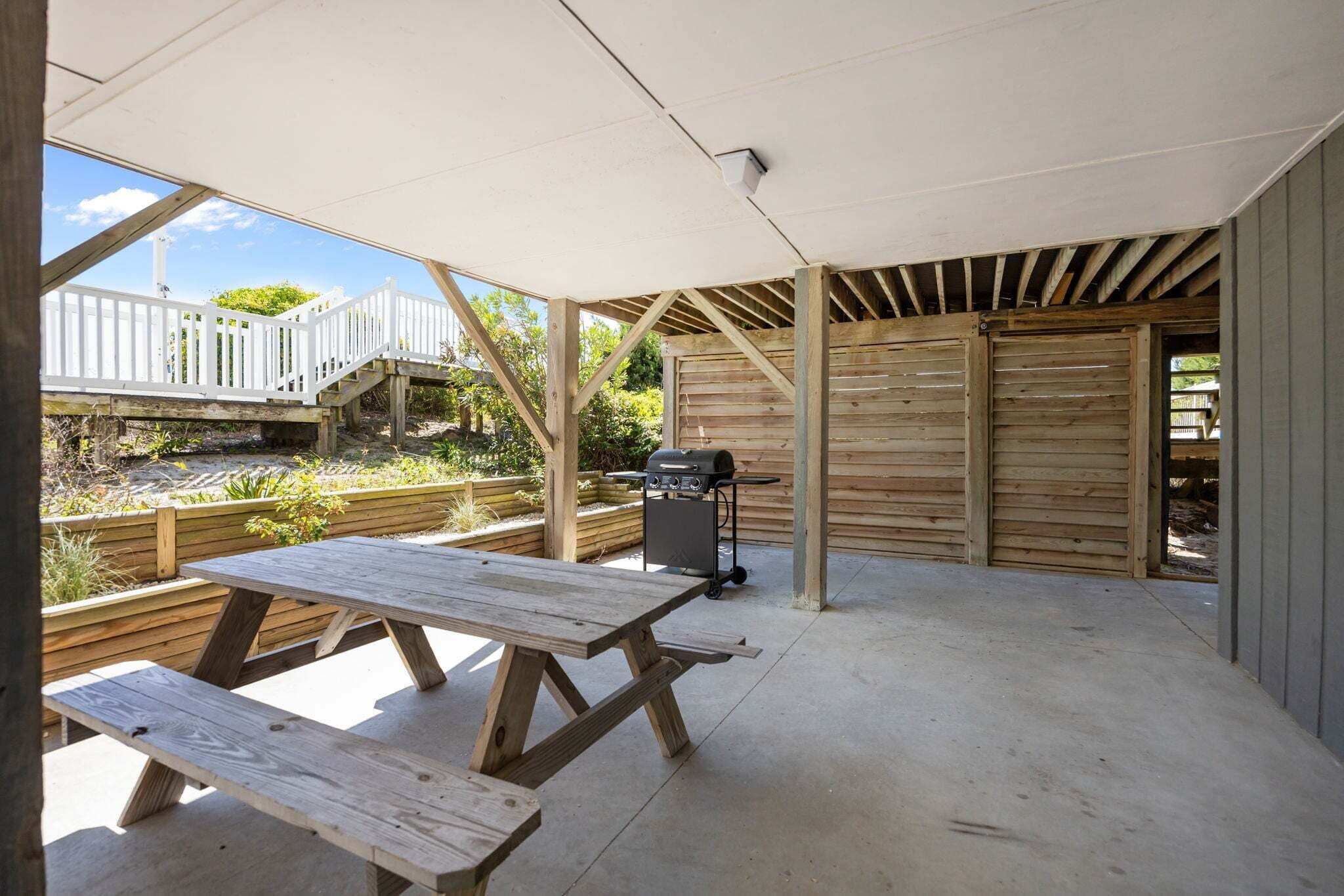An outdoor patio area with picnic tables, a barbecue grill, and a wooden deck.
