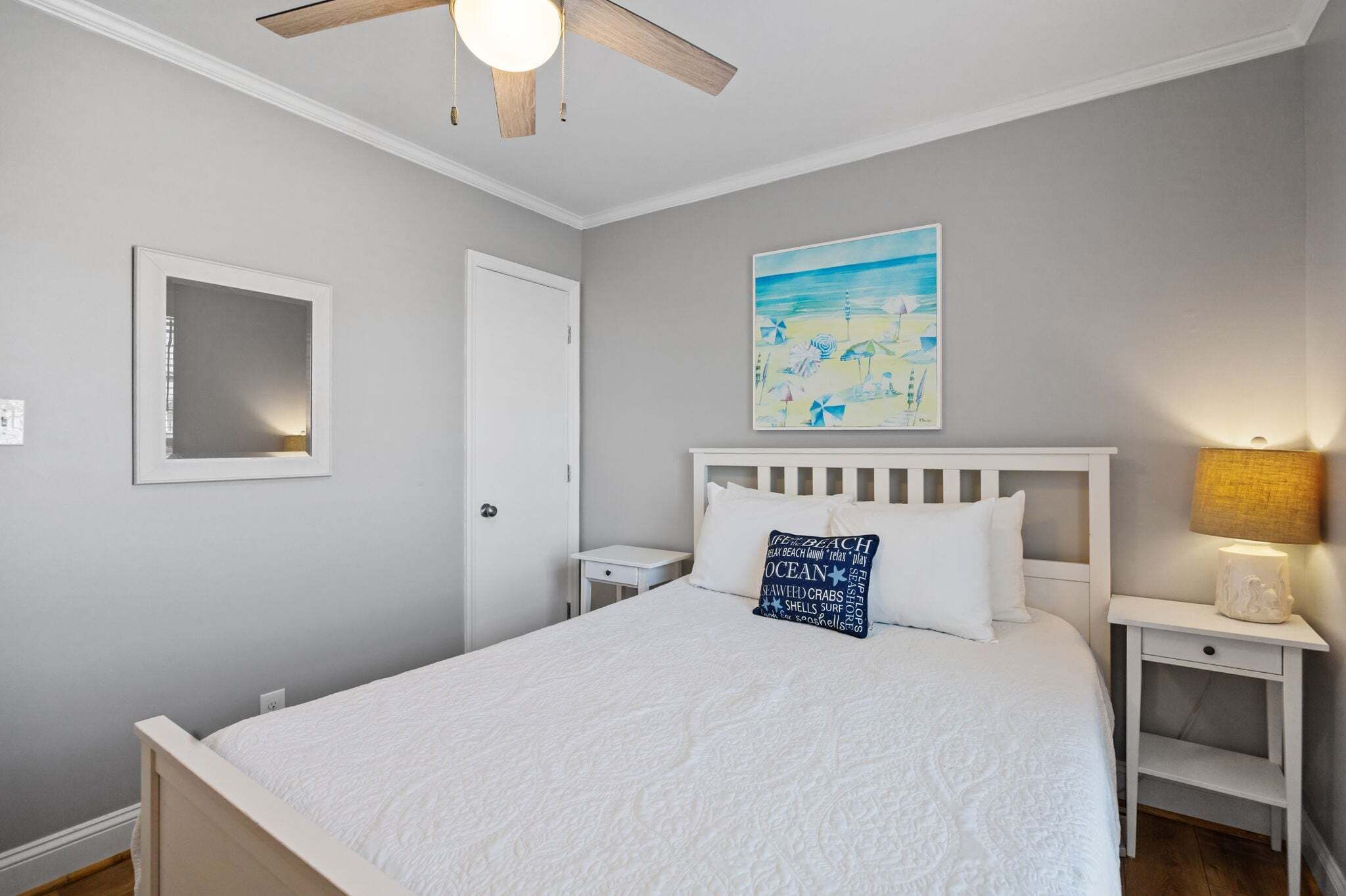 Een slaapkamer met een bed, een plafondventilator, een nachtkastje, een lamp, een schilderij en een spiegel.