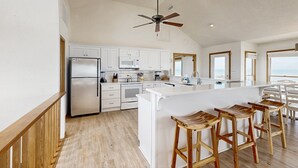 A modern kitchen with white cabinetry, a built-in microwave, and a large island with bar stools. - Prime Time 222: Oceanfront w/outdoor pool, private hot tub, basketball (Avon)