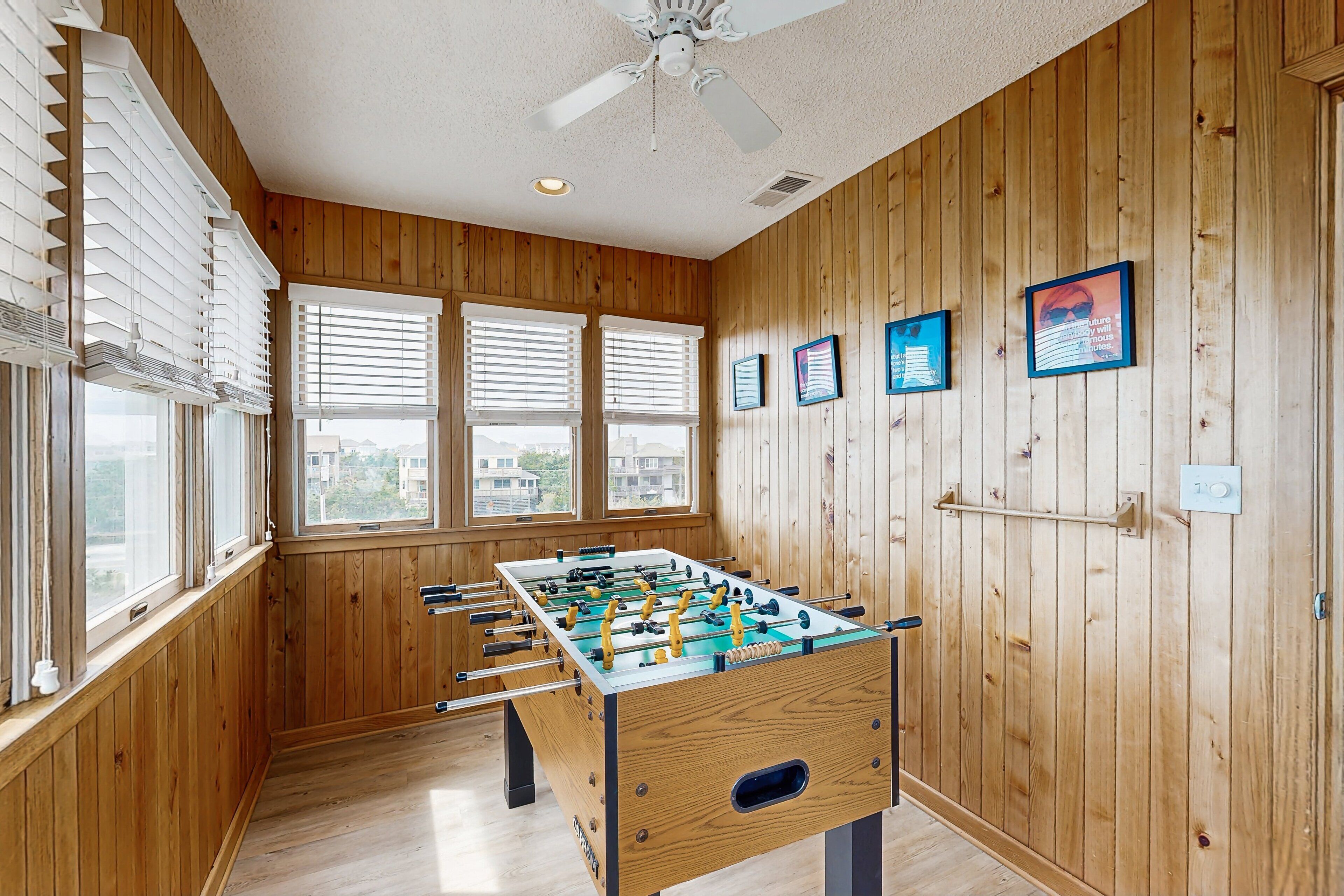 Een kamer met houten wanden, een tafelvoetbaltafel en grote ramen met zonwering.