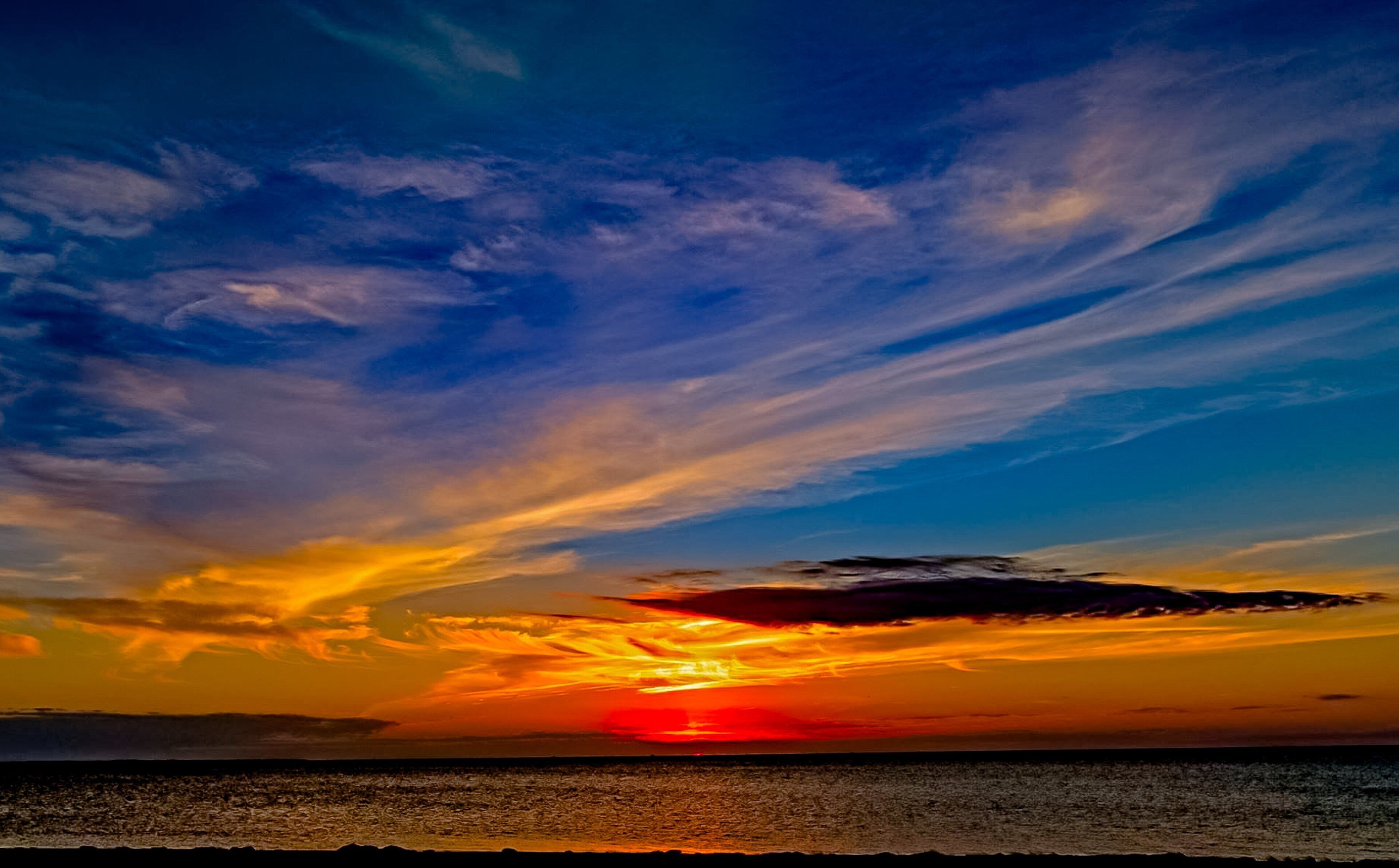 Atardecer sobre un cuerpo de agua con cielo despejado y nubes.