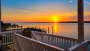 Ein Sonnenuntergangsblick von einem Balkon mit Holzdeck und einem Steg, der sich ins Wasser erstreckt.
