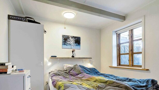 Ett sovrum med en säng, ett skrivbord, ett fönster och en tavla på väggen.