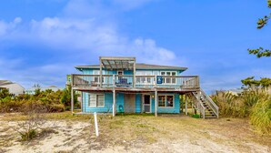 Une maison de plage à deux étages, dotée d’un balcon et d’une véranda couverte.